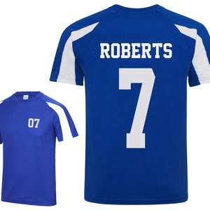 May include: Two blue athletic shirts. One shirt has the number "07" on the front. The other shirt has the name "ROBERTS" and the number "7" on the back. Both shirts have white accents on the shoulders and sleeves.