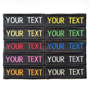 May include: A selection of black rectangular patches, each embroidered with the text "YOUR TEXT" in a range of colours. The embroidery colours include white, yellow, green, red, blue, pink, and orange. The patches are arranged in a grid.