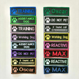 Peut inclure: Plusieurs écussons brodés pour chiens, avec des textes et des empreintes de pattes. On y trouve des phrases comme "TRAINING", "ASSISTANCE DOG", et "DO NOT PET". Les noms "Oscar" et "MAX" sont également présents. Chaque écusson a un code couleur différent.