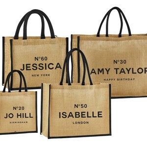 May include: Four brown burlap tote bags with black handles and black trim. The bags are personalised with names and numbers. The bags read "N°60 Jessica New York", "N°30 Amy Taylor Happy Birthday", "N°20 Jo Hill Birmingham", and "N°50 Isabelle London".