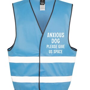 May include: A light blue vest with black trim and two white reflective stripes. The text "ANXIOUS DOG PLEASE GIVE US SPACE" is printed in white on the front. The vest is designed for dogs.