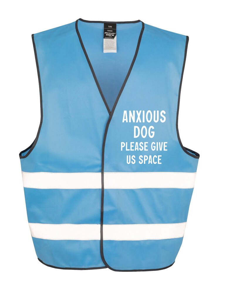May include: A light blue vest with black trim and two white reflective stripes. The text "ANXIOUS DOG PLEASE GIVE US SPACE" is printed in white on the front. The vest is designed for dogs.