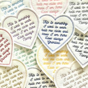 May include: A set of three ceramic mugs with a speckled, cream-coloured glaze. Each mug features a different hand-painted design: a blue and green leaf, a yellow flower, and a red berry. The mugs have a simple, modern design.