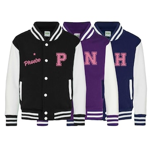 Peut inclure: Trois vestes universitaires noires, violettes et bleu marine. Chaque veste a des manches blanches et un col blanc. La veste noire porte le nom "Phoebe" et la lettre "P" en rose. La veste violette porte la lettre "N" en rose, et la veste marine porte la lettre "H" en rose.