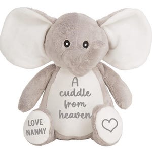May include: A grey plush elephant with large white ears. The elephant has a white patch on its chest with the text "A cuddle from heaven" and a heart on its right foot. The left foot has the text "LOVE NANNY".