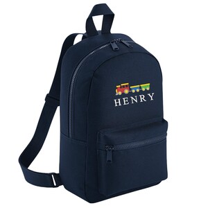 May include: Navy blue backpack with a front zippered pocket and adjustable straps. The backpack features a colorful train graphic and the name "HENRY" embroidered in white. The backpack has a top handle and two zippered compartments.
