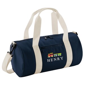 May include: Navy blue duffel bag with cream-colored handles and shoulder strap. Features a colorful train graphic and the name "HENRY" embroidered in white. Includes a zippered main compartment and a front pocket.
