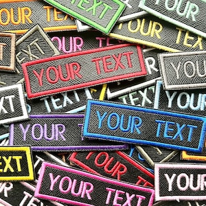May include: A pile of embroidered patches, each with the words "YOUR TEXT" and "OUR TEXT". The patches are rectangular with coloured borders and embroidered lettering, suitable for customisation.