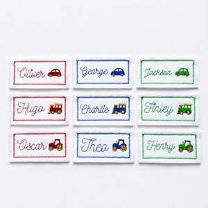 May include: Nine rectangular white fabric labels with embroidered borders and names in red, blue, or green thread. Each label features a matching embroidered vehicle icon, including cars, trains, and tractors, next to names like Oliver, George, and Jackson.