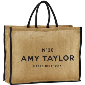 May include: A brown burlap tote bag with black handles and trim. The bag has the text "N&deg;30 AMY TAYLOR HAPPY BIRTHDAY" printed on the front.