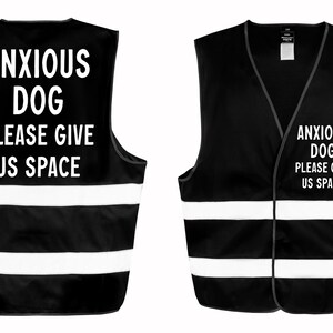 May include: Black vest with white reflective stripes and the text "ANXIOUS DOG PLEASE GIVE US SPACE" in white. The vest is designed to be worn by a dog. The image shows the front and back of the vest.