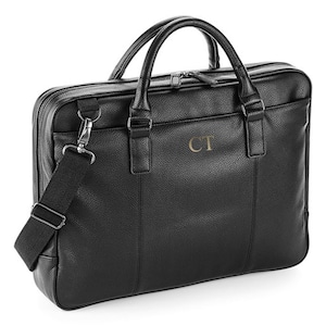 May include: Black leather briefcase with a shoulder strap and a zipper closure. The briefcase has a gold embossed monogram "CT" on the front.