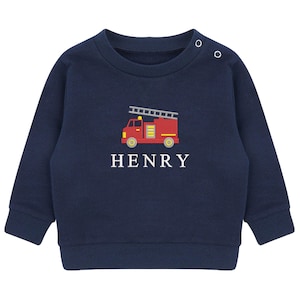 May include: Navy blue baby sweatshirt with a red fire truck graphic and the name "HENRY" embroidered in white. The fire truck has a yellow ladder, wheels, and lights. The sweatshirt has two buttons on the shoulder.
