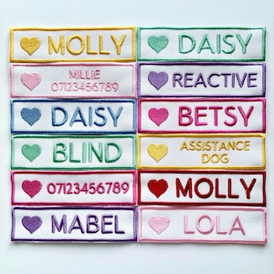 May include: Embroidered patches with names and text, including "MOLLY," "DAISY," and "ASSISTANCE DOG." Each patch features a heart symbol and is framed with a colored border. The patches are white with colorful embroidery.