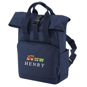 May include: Navy blue backpack with a roll-top closure and a black buckle. The front pocket features a colorful train graphic and the name "HENRY" embroidered in white. Includes a side pocket and adjustable straps.