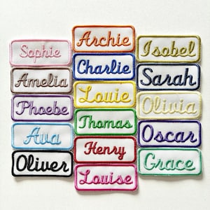 May include: A selection of embroidered name patches in various colours. Each patch displays a different name in a cursive font, including "Sophie", "Archie", "Isobel", "Amelia", "Charlie", "Sarah", "Louie", "Phoebe", "Olivia", "Ava", "Oscar", "Oliver", "Henry", "Grace", and "Louise".
