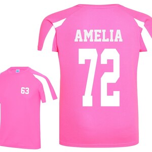 May include: Two pink athletic shirts with white accents. One shirt displays the number "63" in white, while the other features the name "AMELIA" and the number "72" in white. The shirts have a crew neck and short sleeves.