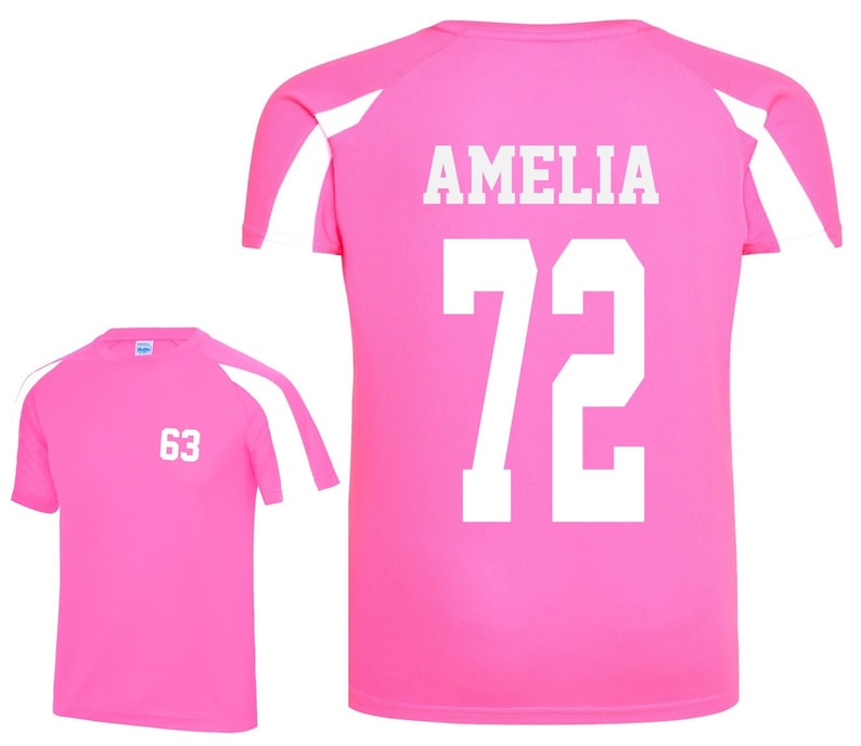 May include: Two pink athletic shirts with white accents. One shirt displays the number "63" in white, while the other features the name "AMELIA" and the number "72" in white. The shirts have a crew neck and short sleeves.