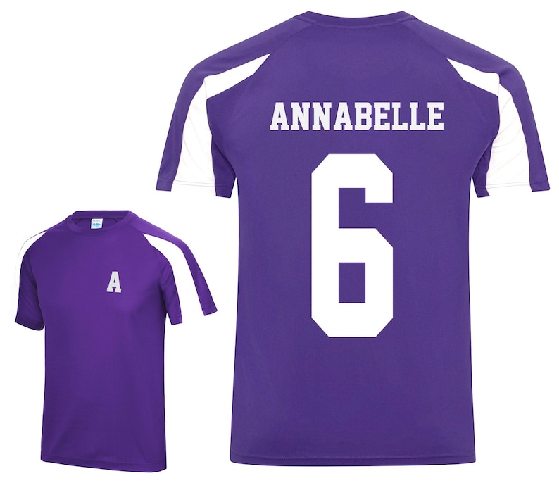 May include: Purple athletic shirt with white shoulder accents. The back of the shirt displays the name "ANNABELLE" and the number "6" in white block letters. A smaller shirt with the letter "A" is also shown.