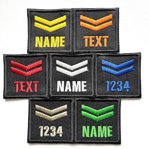May include: A collection of black embroidered patches with chevron designs in various colors, including yellow, orange, red, white, blue, tan, and green. Each patch features text or numbers, such as "NAME", "TEXT", and "1234".