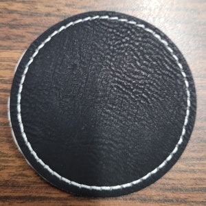 May include: Black round leather coaster with white stitching around the edge.