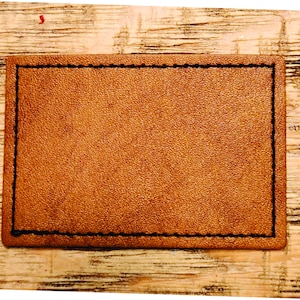 May include: A brown leather label with a stitched border. The label is on a wood background.
