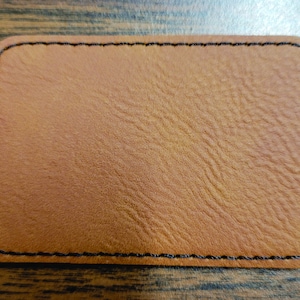 May include: A brown leather patch with black stitching around the edges.