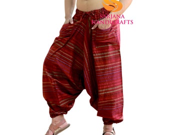 May include: A man wearing red and white striped pants with a drawstring waist. The pants have a pocket on the side. The man is standing with his hands in his pockets. The pants are made by Sarjana Handicrafts.