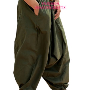 May include: A pair of olive green loose-fitting pants with a drawstring waist and a small pocket on the left side. The pants are gathered at the ankles and the model is wearing brown sandals.