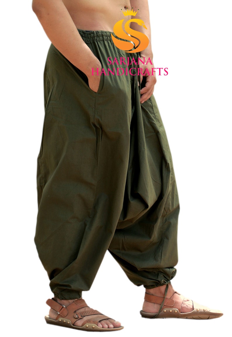 May include: A pair of olive green loose-fitting pants with a drawstring waist and a small pocket on the left side. The pants are gathered at the ankles and the model is wearing brown sandals.