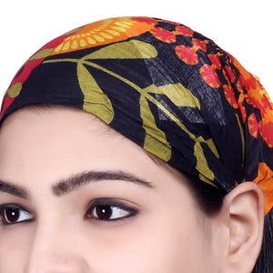 May include: A black headscarf featuring a vibrant floral design in shades of orange, yellow, and green. The headscarf is made from a soft, lightweight material and is worn on the head. The floral pattern adds a touch of colour and style.