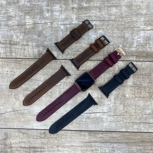 May include: Five different watch bands, including brown, dark brown, burgundy, and black leather bands, and a black silicone band. The bands are arranged in a star shape on a wooden surface.