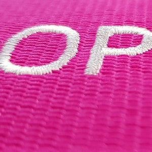 The image showcases an pink luggage strap with the name embroidered in large, white letters. The strap is bright colour enhances visibility, and the bold lettering personalizes the item, making it easier for the owner to identify their luggage.