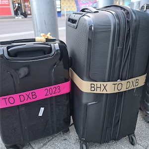 two suitcases side by side on a sidewalkat an airport. Both straps appear to be custom-made to indicate travel plans, he surroundings suggest the luggage owners are either departing from or arriving at a travel hub.