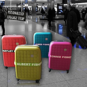 photo showing four colorful suitcases with personalized luggage straps. The suitcases are red, blue, yellow, and pink, and each strap is printed with a different name. The suitcases are set against a black and white background of an airport setting