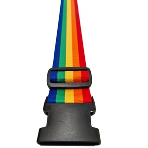 The image features a rainbow-colored strap with a black plastic buckle, typically used for securing items like luggage. The vibrant strap displays the full spectrum of rainbow colours in vertical stripes, and the traditional rainbow sequence.