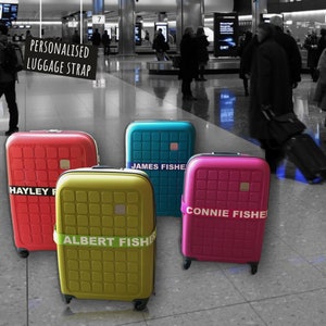 photo showing four colourful suitcases with personalized luggage straps. The suitcases are red, blue, yellow, and pink, and each strap is printed with a different name. The suitcases are set against a black and white background of an airport setting