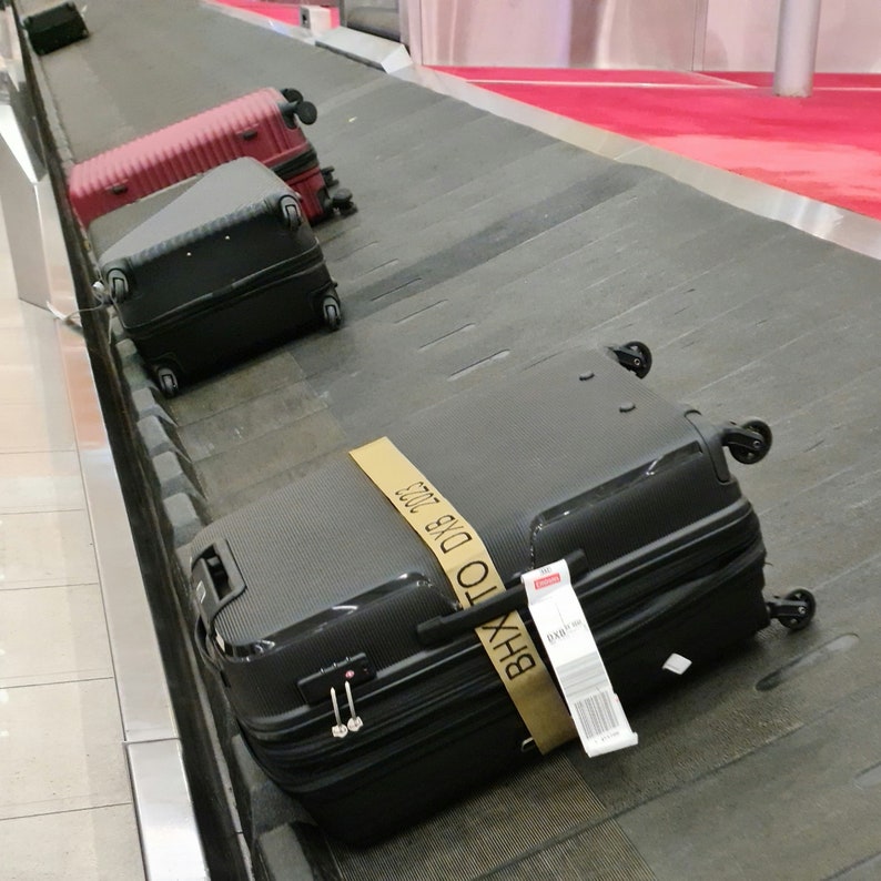 luggage on airport carousel with personalised luggage strap showing how it stands out compared to a luggage without the strap.