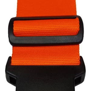 The image features a orange -coloured strap with a black plastic buckle, typically used for securing items like luggage.
