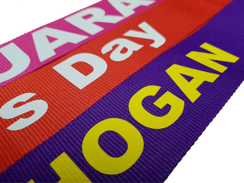 The image showcases an pink, red, purple luggage strap with the names printed. The strap is bright colour enhances visibility, and the bold lettering personalizes the item, making it easier for the owner to identify their luggage.