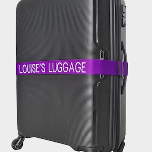 Könnte beinhalten: Schwarzer Koffer mit einem violetten Gepäckband, auf dem "LOUISE'S LUGGAGE" in weißen Buchstaben steht.