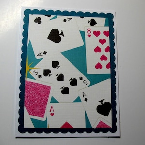 May include: A rectangular greeting card featuring a scalloped dark blue border. The center design displays a collage of playing cards with black spades, pink hearts, and a pink patterned card back against a bright teal background with a yellow star.