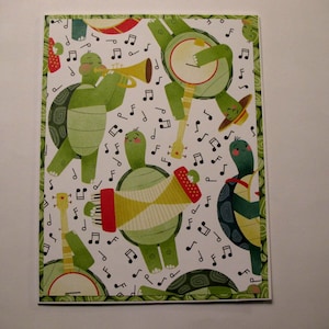 May include: A whimsical illustration features a band of green turtles playing musical instruments. The turtles are depicted with smiling faces and are surrounded by musical notes. The instruments include a trumpet, banjo, guitar, and accordion. The border has a green and red pattern.