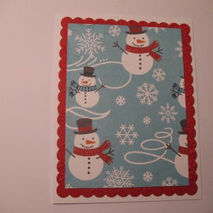 May include: A red and white scalloped border card with a blue background featuring a winter scene with snowmen and snowflakes. The snowmen are wearing scarves and hats.