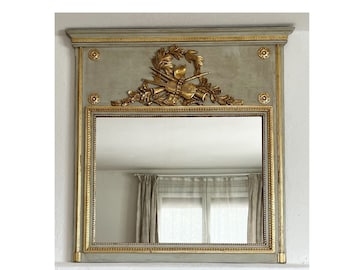 Puede incluir: Un espejo antiguo gris y dorado con un marco tallado decorativo. El marco presenta un diseño floral con un motivo central de cuernos de caza cruzados y una corona de laurel.