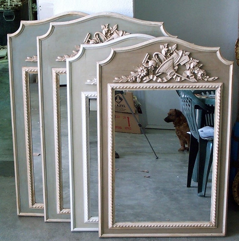 May include: Four rectangular mirrors with decorative frames. Each mirror has a floral and ribbon design at the top. The frames are a muted green and beige, with a rope-like border. The mirrors are likely for home decor.