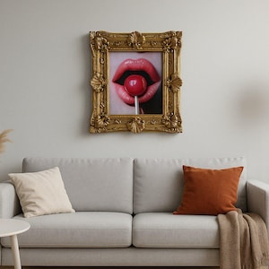 Könnte beinhalten: Ein gerahmter Druck eines Mundes mit einem roten Lutscher, über einem grauen Sofa mit orangefarbenen und cremefarbenen Kissen. Der verzierte goldene Rahmen verleiht dem Kunstwerk einen Vintage-Touch. Eine Stehlampe und eine Vase mit Ziergras vervollständigen den Raum.