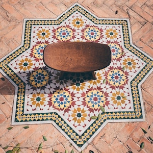 May include: A wooden stool with a rounded top sits in the center of a star-shaped tile floor. The tiles are white with yellow, blue, and red geometric patterns.