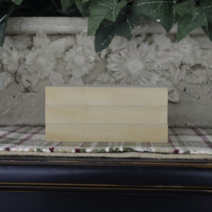 May include: A stack of three unfinished wooden blocks, each with a smooth, light brown surface. The blocks are arranged in a rectangular shape and are sitting on a plaid fabric surface.