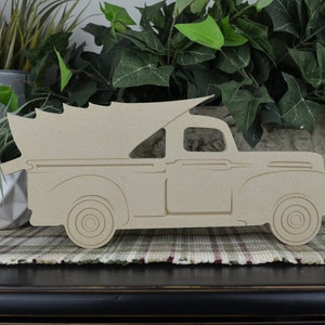 K&ouml;nnte beinhalten: Ein Holzausschnitt eines Vintage-Pickups mit einem Weihnachtsbaum in der Ladefl&auml;che. Der LKW ist in hellbraun lackiert und nach rechts gerichtet. Der LKW steht auf einer karierten Oberfl&auml;che.